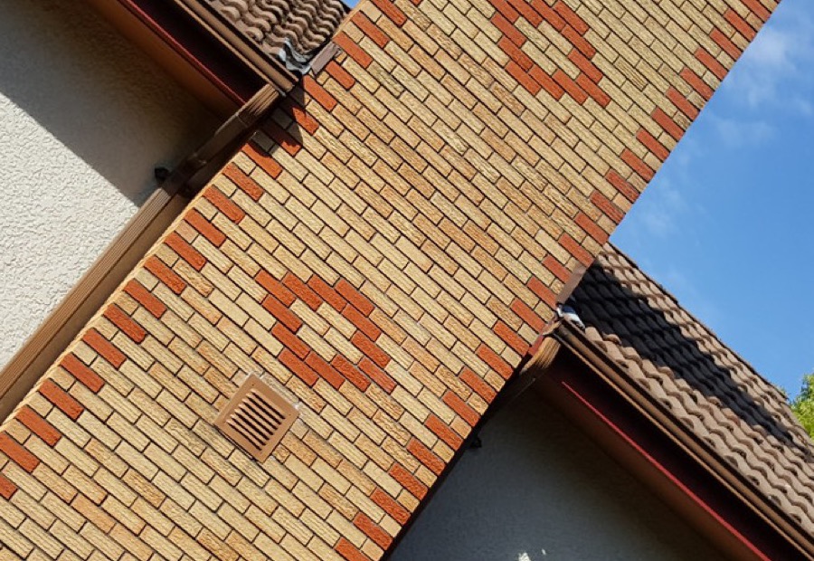 Brick chimney above a roofline with a cracked crown and spalling brick